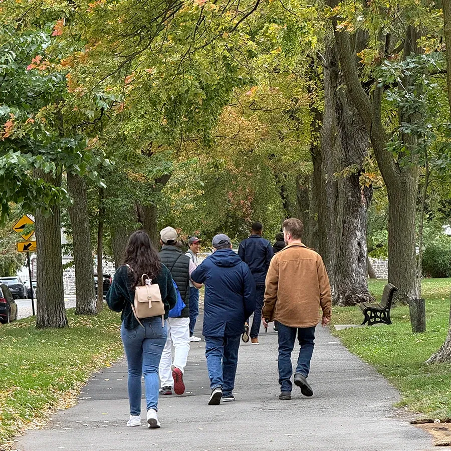 Teammates seen from behind walking down a tree-lined path in a park, with autumn leaves starting to turn.