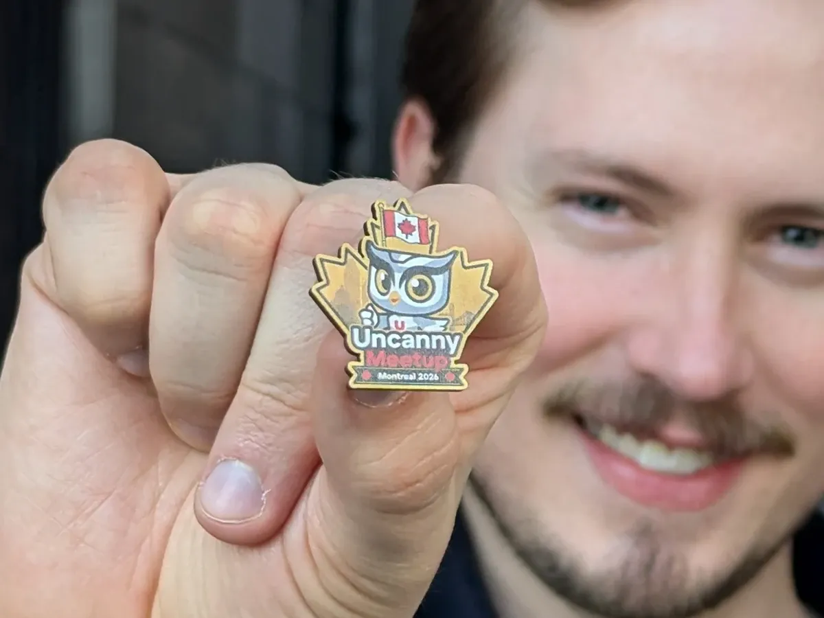 Agustin Barrientos holding up the trip's pin, a maple leaf with the company's owl mascot, a Canadian flag, and the words Uncanny Meetup Montreal 2026.