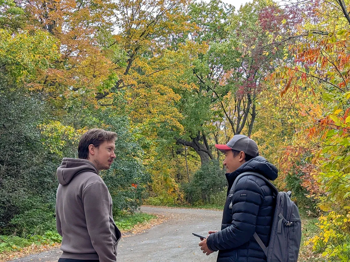 Agustin Barrientos (left) and Ken Young (right) talking face to face on a path through autumn woods, in Montreal, Canada
